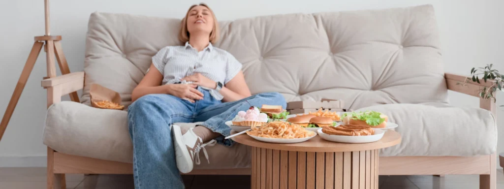 Woman relaxing on a beige sofa with a round wooden coffee table full of snacks in front of her.