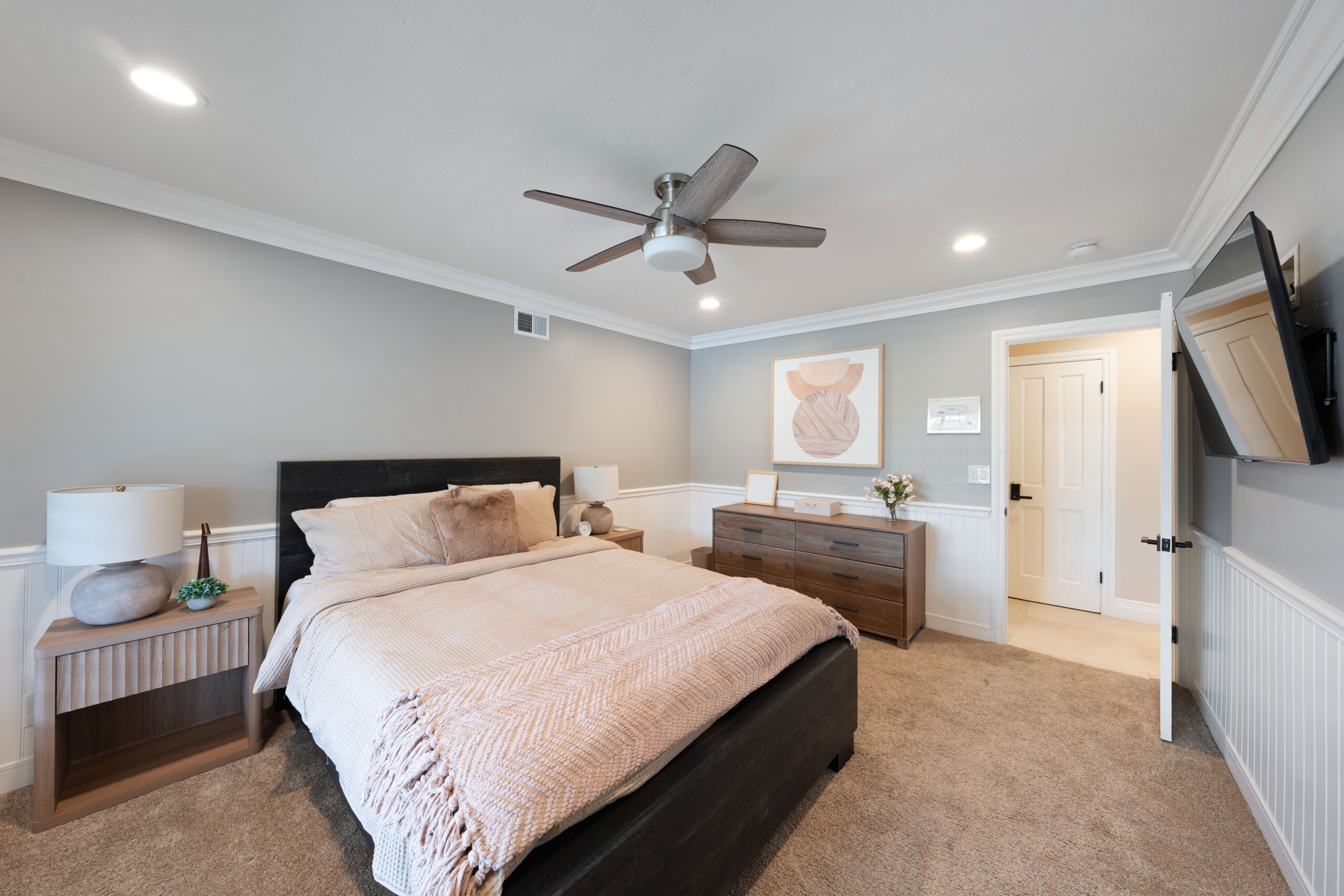Bedroom with dark wooden bed, beige bedding, two matching nightstands, and a ceiling fan on a gray wall.