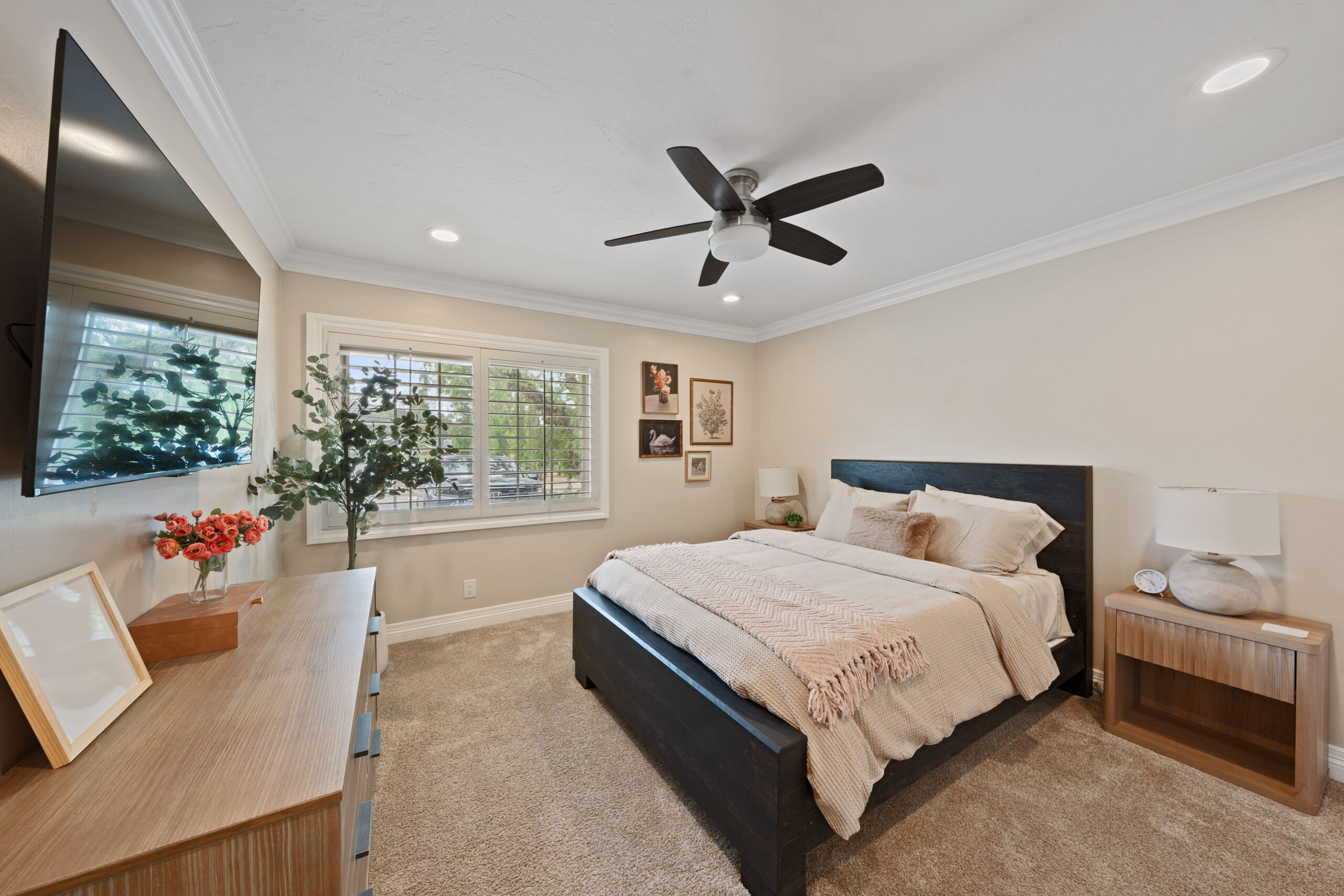 Bedroom interior with dark wood platform bed, beige bedding, ceiling fan, and large window with blinds