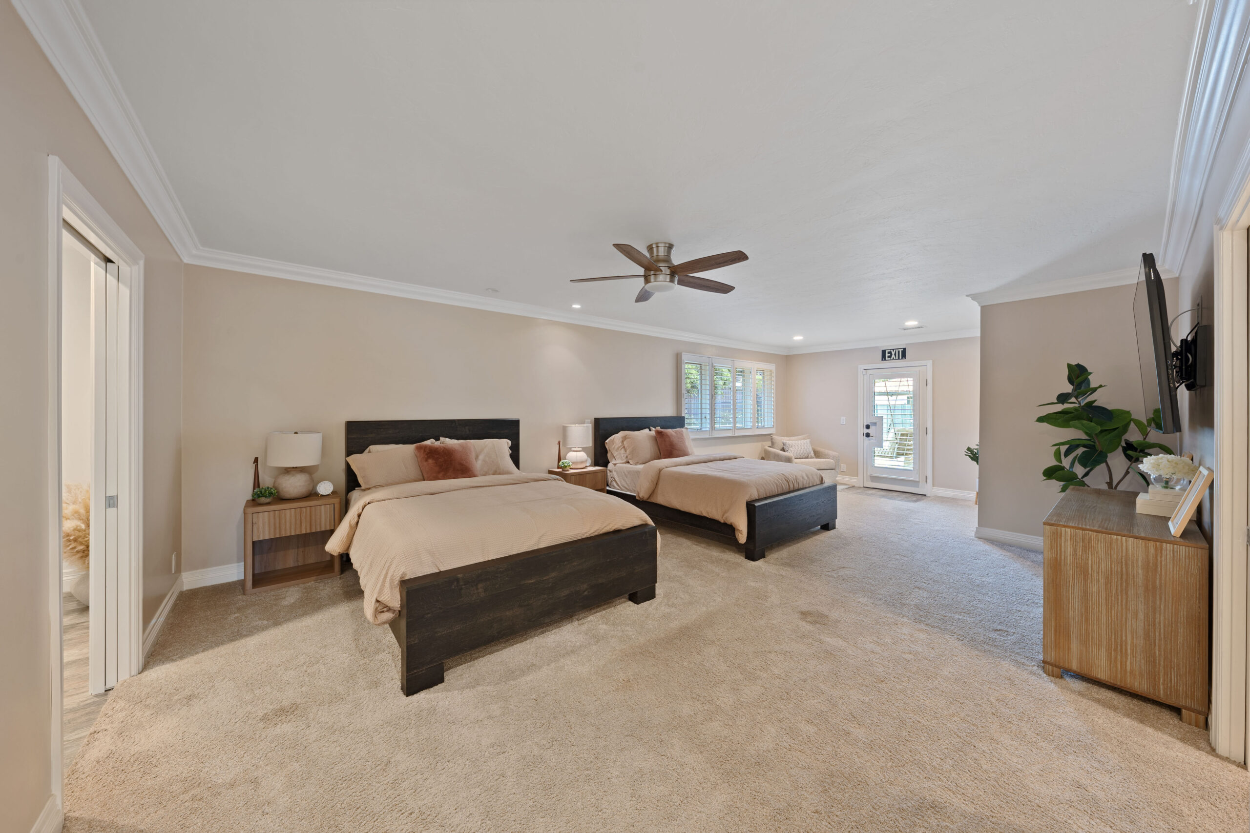 Hotel-style master bedroom with two dark wood platform beds, beige bedding, and matching nightstands under a vaulted ceiling with a ceiling fan.