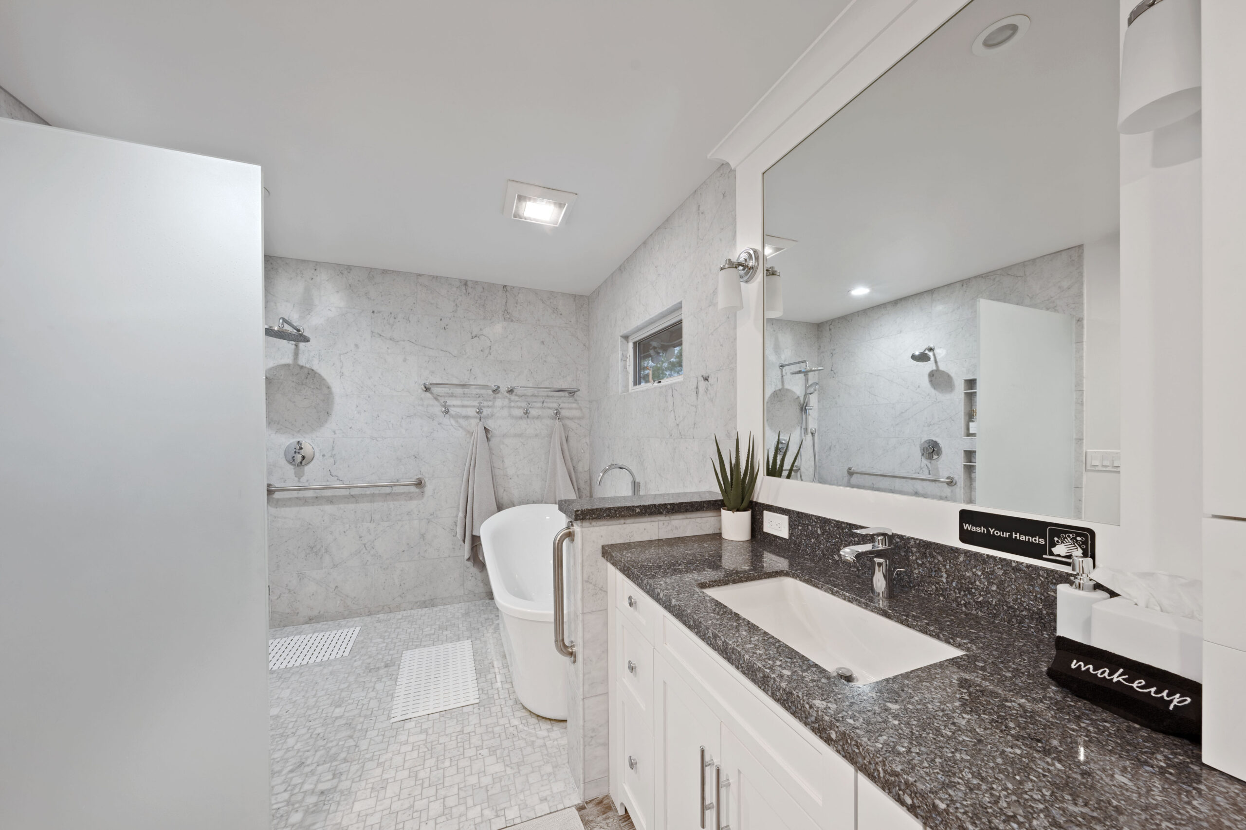 Bright modern bathroom with marble walls, white vanity, dark granite countertop, and a large mirror.