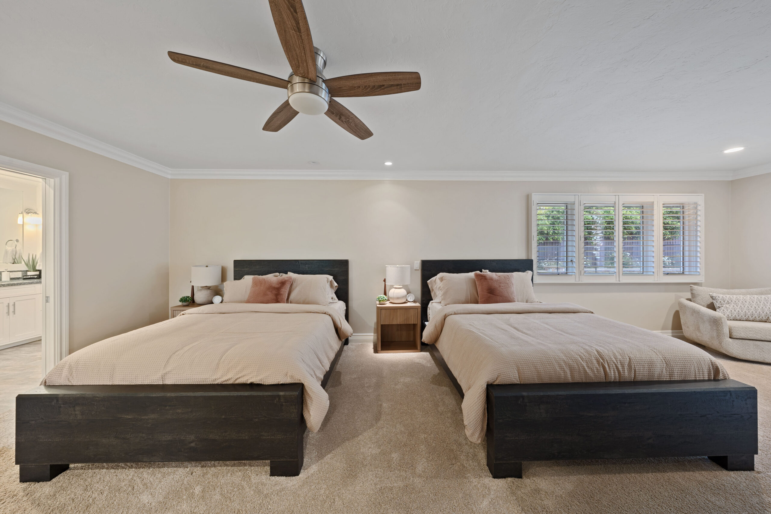 Bedroom with two queen beds on dark wooden platforms, beige bedding, and matching nightstands under a ceiling fan.