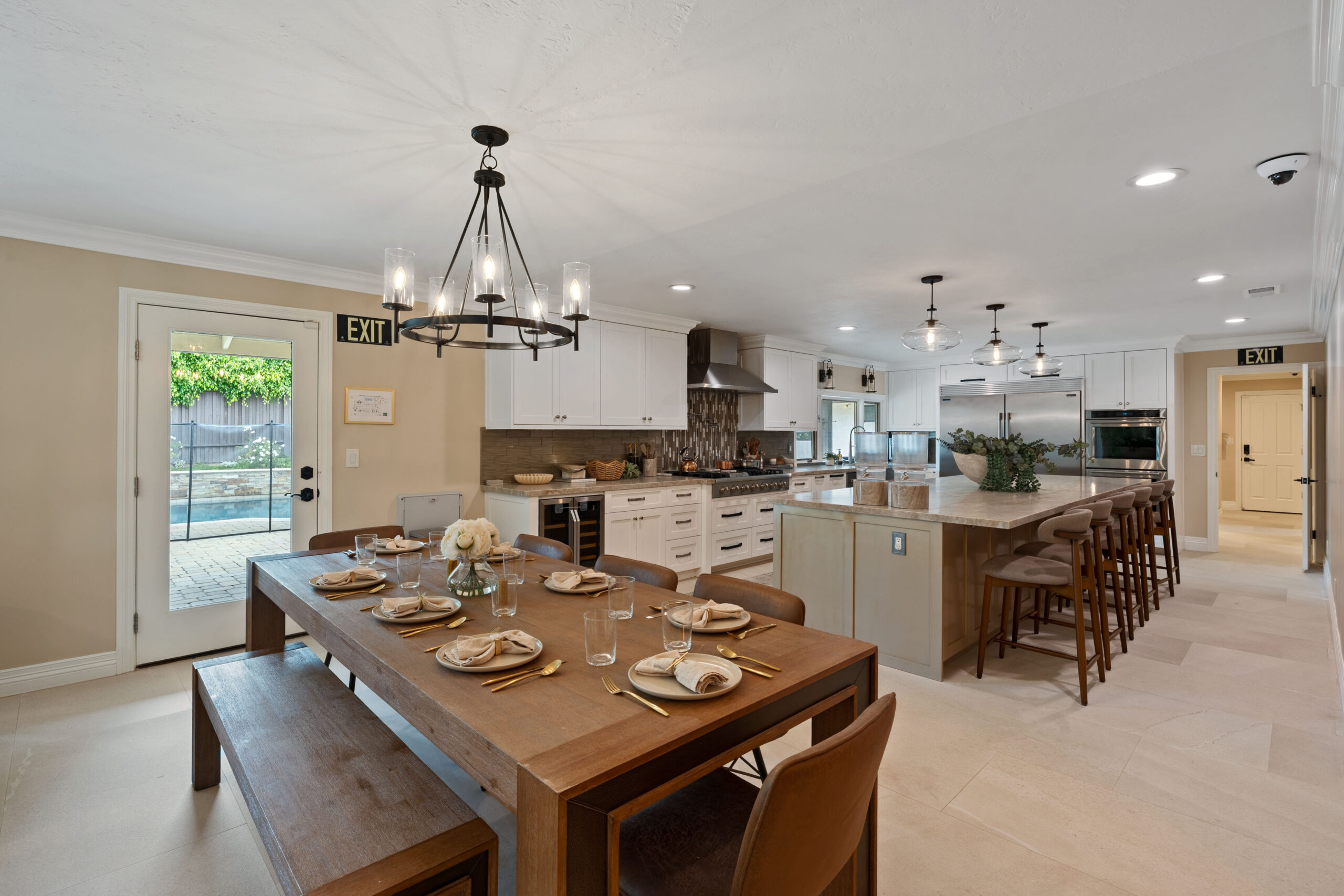 Open-plan kitchen and dining area with wooden table set for six, a chandelier, white cabinets, and an island.
