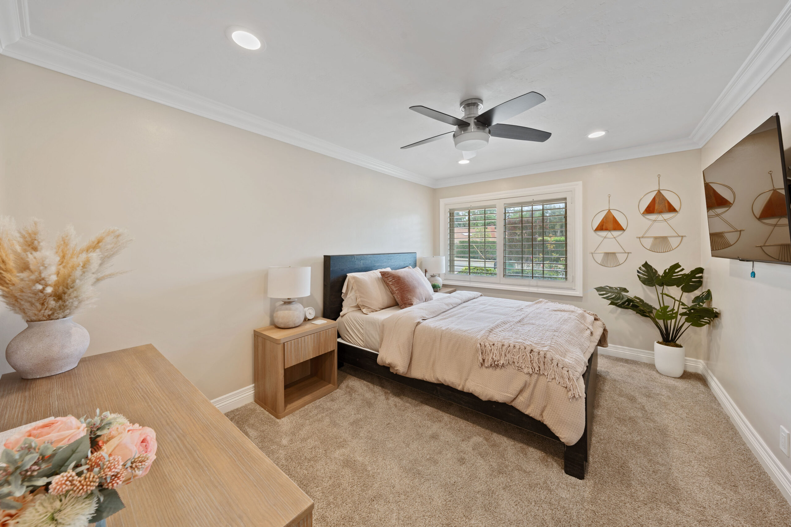Cozy bedroom with a dark wood bed, beige linens, two wooden nightstands, and a ceiling fan above; window with blinds to the right.